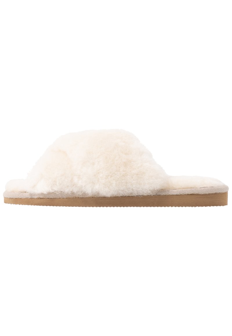 Pluizige crèmekleurige slipper met een zachte bovenkant, een platte zool en een getextureerde tan onderkant. Eenvoudig open teen ontwerp zonder extra hardware.