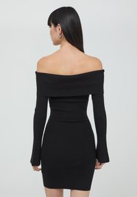 Abito nero a coste con spalle scoperte, maniche lunghe e aderenti e una silhouette snella, caratterizzato da un scollo dritto e un tessuto testurizzato.