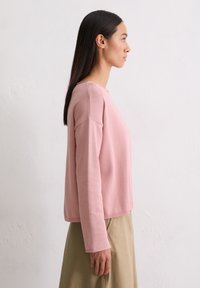 Lichtroze sweatshirt met lange mouwen, ronde halslijn en een zachte textuur. Gestyled met een beige rok, bekeken vanuit de zijkant.