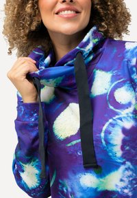 Sudadera con capucha en púrpura con patrones abstractos en azul y blanco. Presenta un cuello alto y cuerdas negras para ajuste. Textura suave.