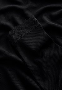 Tela negra acanalada con un borde superior de encaje texturizado, de apariencia suave y lisa, doblada y colocada sobre una superficie oscura.