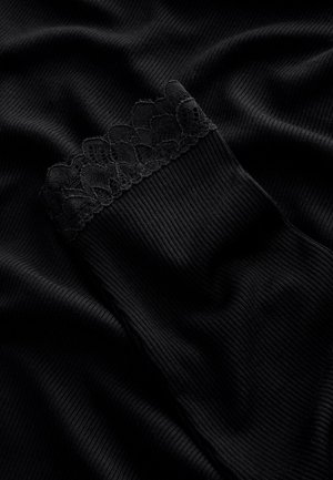 Svart ribbad tyg med en texturerad spetskant upptill, slät och mjuk yta, vikt och draperad på en mörk yta.