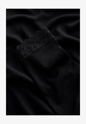 Czarny prążkowany materiał z teksturowaną koronkową wstawką u góry, gładki i miękki w wyglądzie, złożony i ułożony na ciemnej powierzchni.