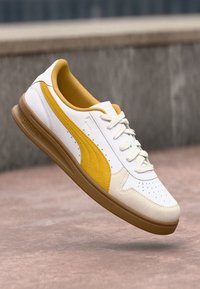 Hvit og gul sneaker med perforert tåboks, myk gul foring, teksturert hvit læroverdel og lys brun gummi såle.