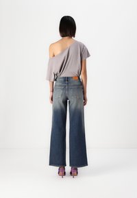 Grå av-og-til-top, vide falmede denimjeans med lærlabel, kombinert med lilla høyhælte sko. Minimalistisk bakgrunn.