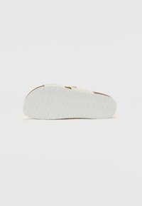 Hvid sål med bølgende tekstur, der viser en glat overflade; overdelen har en lys cremefarve med brune accenter og minimalistiske designelementer.