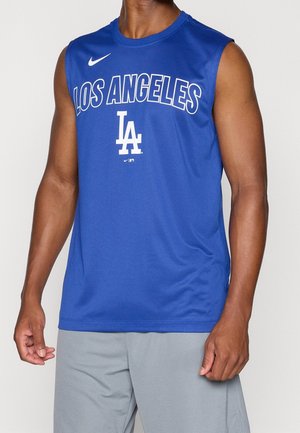 Mann trägt blaues ärmelloses Sportshirt von Los Angeles und graue Shorts, steht vor einfarbigem Hintergrund.