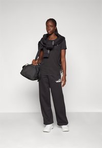 Black athletic outfit featuring a short-sleeve top and loose-fit pants. The top has a logo, with a coordinating black bag and white sneakers.