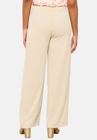 Beige wijde broek met een elastische tailleband, gladde textuur en een lichtgewicht stof, gecombineerd met beige schoenen met blokhak.