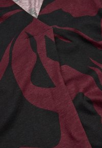 T-shirt med en svart och mörkröd design med abstrakta, flytande mönster. Tillverkad av mjuk bomull, den har en slät textur.