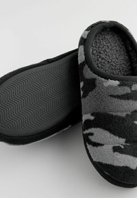 Chaussons en tissu camouflage noir et gris avec une tige en polaire douce, une semelle en caoutchouc noir texturé et un intérieur douillet.