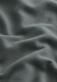 Tissu doux et lisse en gris atténué, délicatement plié avec des ombres subtiles mettant en valeur la texture et les détails du tissage.