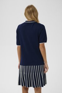 Jūrų laivyno suknelė su prigludusia viršutine dalimi ir klostuota, raižyta sijona. Turi trumpas rankoves ir kontrastingą apykaklę. Minkšta medžiagos tekstūra.