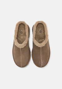 Chaussons marron à enfiler avec une doublure douce et duveteuse et le logo UGG à l'intérieur, détail cousu au centre, vus de dessus sur fond blanc.