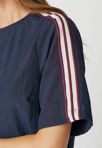 Navyblauwe top met korte mouwen en rode, witte en blauwe gestreepte accenten op de schouders; gestructureerde stof met een ontspannen pasvorm.