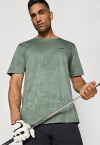 T-shirt vert à manches courtes avec un motif à carreaux et le logo "BOSS", accompagné d'un gant de golf blanc tenant un club.