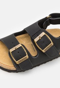 Svart skinne sandaler med to justerbare stropper med messingspenner og en kork såle. Strukturert yttersåle for grep og komfort.