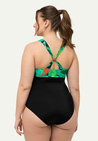 Maillot de bain une pièce avec un haut vert et noir à motifs abstraits, des bretelles réglables et un bas noir uni. Tissu lisse et extensible.