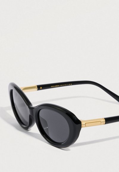 Μαύρα υπερμεγέθη γυαλιά ηλίου με κυρτούς φακούς, γυαλιστερά μαύρα πλαίσια και ναούς με χρυσές λεπτομέρειες. Μινιμαλιστικός σχεδιασμός χωρίς μοτίβα.