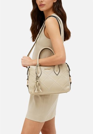 Borsa trapuntata beige con dettagli neri, doppie maniglie e un nappina decorativa. Dettaglio logo dorato sul davanti. Texture in pelle liscia.