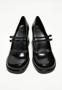 Black patent leather heels with a rounded toe, featuring two cross-strap buckles, smooth texture, and a chunky platform sole.
