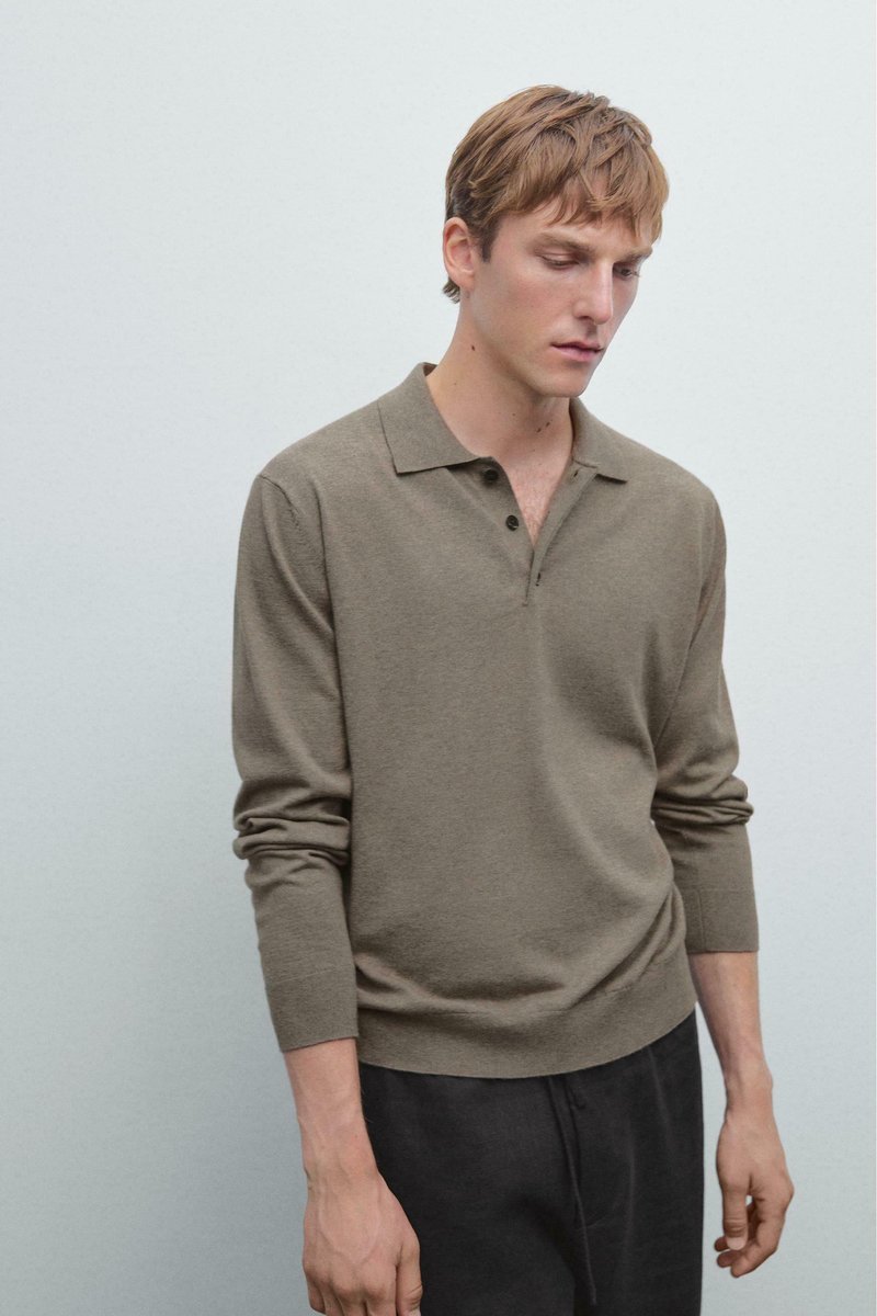 Jonge man met lichtbruin haar in een bruine lange mouw polo en donkere broek voor een effen lichtgrijze achtergrond.