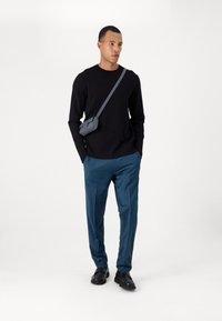 Pull en maille noir, pantalon turquoise, chaussures noires et sac bandoulière gris. Design minimaliste avec des lignes épurées et une silhouette ajustée.