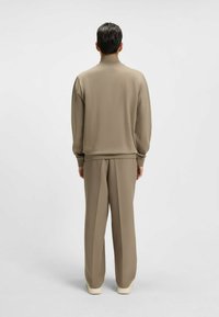 Beige tracksuit with a high collar, soft texture, and relaxed fit. The pants are wide-legged, paired with light-colored footwear.