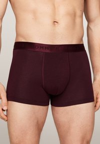 Burgundske bokserice z ujemajočim elastičnim pasom, ki ima izbočeno blagovno znamko. Mehak, raztegljiv material s prilegajočim dizajnom.