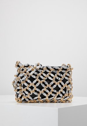 Zwarte clutch tas gewikkeld in een chunky grijze en gouden kettingnet, tentoongesteld op een witte sokkel tegen een eenvoudige grijze achtergrond.