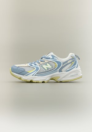 Baskets de sport New Balance 590 blanches et bleu clair avec panneaux en mesh, lacets et semelle texturée, présentées de profil sur fond neutre.