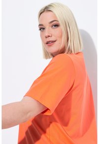 T-shirt a manica corta di un brillante arancione, realizzato in cotone. Presenta una vestibilità rilassata e dettagli di cucitura sulle maniche e sull'orlo.