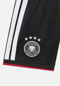 Calções de desporto pretos com riscas laterais brancas e um logótipo circular com uma águia. Acento vermelho perto da bainha. Material suave e leve.