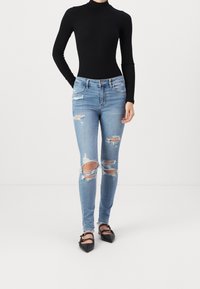 Úzké džíny ve světle modré denimové barvě s roztrženými koleny, spárované s černým body s dlouhým rukávem a černými plochými botami.