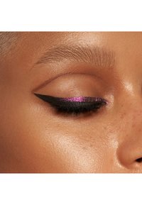 Nærbilde av et øye med svart eyeliner i en skarp vingeform, toppet med en livlig lilla glitterdetalj. Huden har en jevn tekstur.