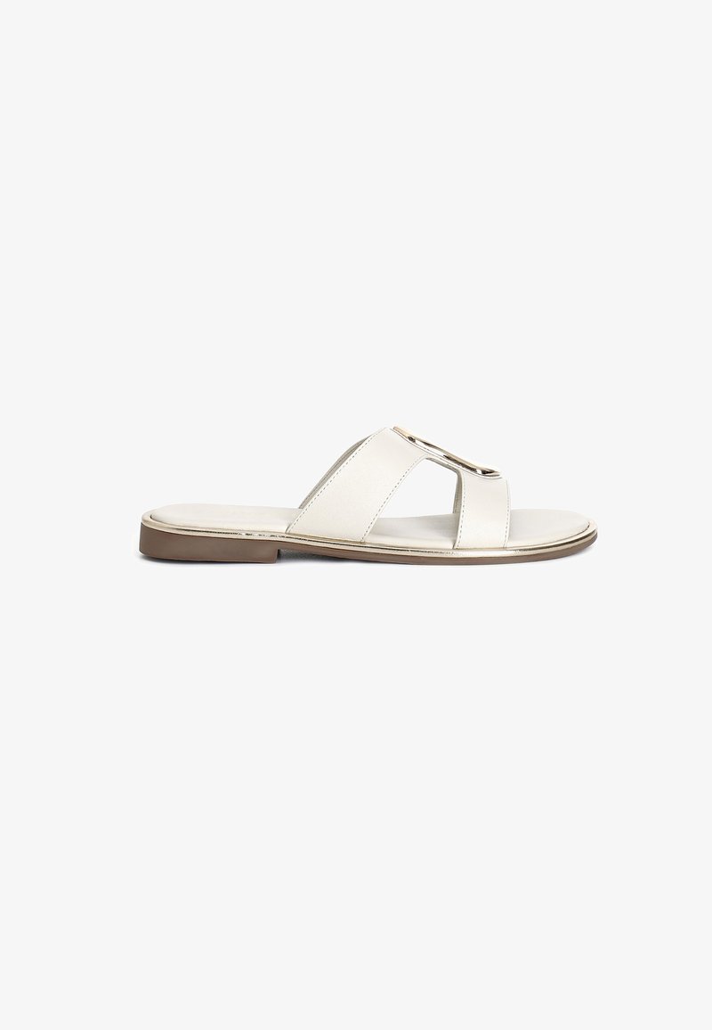 Beige leather slide sandals with a cross strap design and metallic hardware accent. Flat sole with a slight heel.