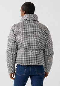 Chaqueta acolchada con un patrón de pata de gallo en blanco y negro, cuello alto y textura acolchada; combinada con vaqueros de mezclilla azul.