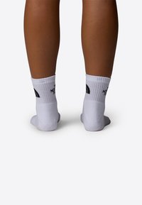 Calcetines deportivos blancos con parte superior acanalada y logo negro en la parte trasera, ajustados al tobillo, mostrando una textura suave.