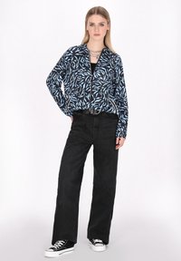 Svart och blå zip-up jacka med vågmönster, ihop med högmidjade svarta raka byxor och svarta sneakers med vita sulor.