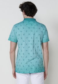 Türkiz színű, rövid ujjú pólóing, finom levélmintával, könnyű anyagból készült, galléros és laza szabású.