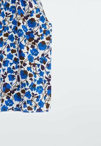 Top senza maniche floreale in tessuto bianco, con motivo di fiori blu e marroni, caratterizzato da un design ampio e fluido e scollatura arrotondata.