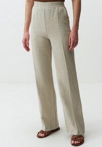Pantaloni in lino beige chiaro con gambe ampia, tessuto testurizzato e vita elastica, abbinati a sandali marroni con cinturini.