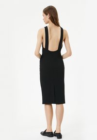 Schwarzes ärmelloses Kleid mit breiten Trägern, tiefem Rückenausschnitt, knielang, tailliertem Design, seitlichem Schlitz, aus glattem Stoff, betonter Silhouette.