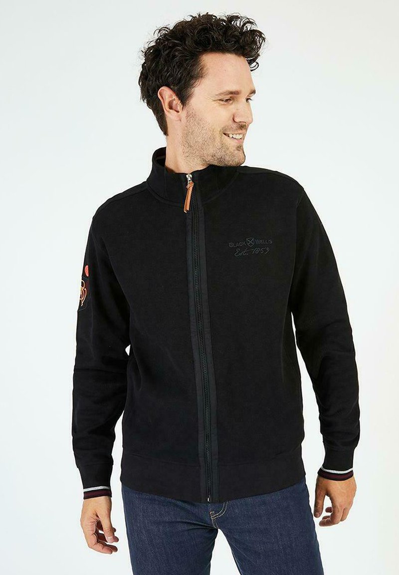 Veste en polaire noire avec col montant, fermeture éclair intégrale sur le devant et tirette orange. Présente un logo brodé et des accents rayés aux poignets.