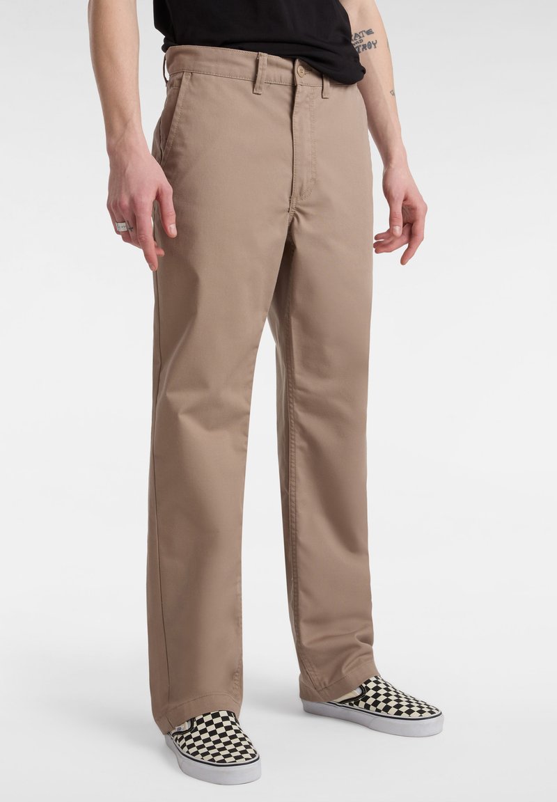 Pantaloni in cotone beige con vestibilità dritta, dotati di chiusura con bottone e tasche laterali a vista, abbinati a scarpe slip-on a scacchi in bianco e nero.