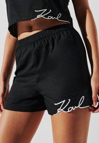 Ensemble de haut cropped noir et de shorts en tissu léger, avec un design fluide et un détail brodé blanc "Karl" sur les shorts.