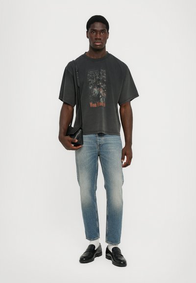 Charcoal oversized t-shirt with graphic print, light blue straight-leg jeans, black loafers, and a small black crossbody bag.
