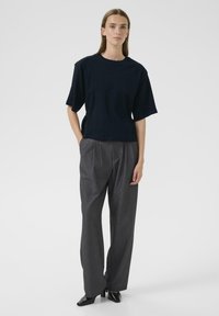 Navyfarbendes, oversized Baumwoll-T-Shirt mit kurzen Ärmeln, kombiniert mit grauen, weit geschnittenen Hosen mit Falten und schwarzen hohen Schuhen.
