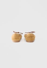 Brown suede moccasin-style shoes with lace detailing and a soft lining, featuring a low-profile sole and stitched accents.