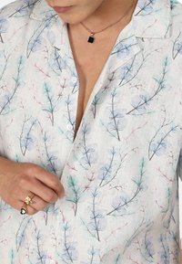 Chemise en lin avec un motif de feuilles pastel en vert, bleu et rose. Dotée d'un col, d'une fermeture à boutons et d'une texture douce. Anneaux décoratifs à la main.